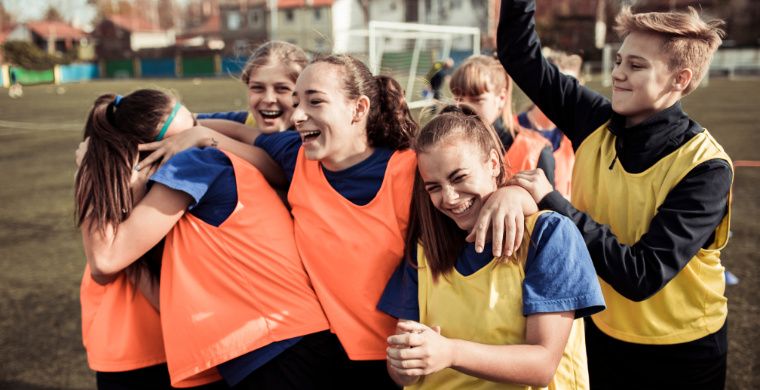 Eine Gruppe Jugendlicher in neonfarbenen Trainingstrikots steht auf einem Fußballplatz und hat Spaß.