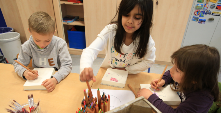 Grundschulkinder sitzen gemeinsam am Tisch und malen.