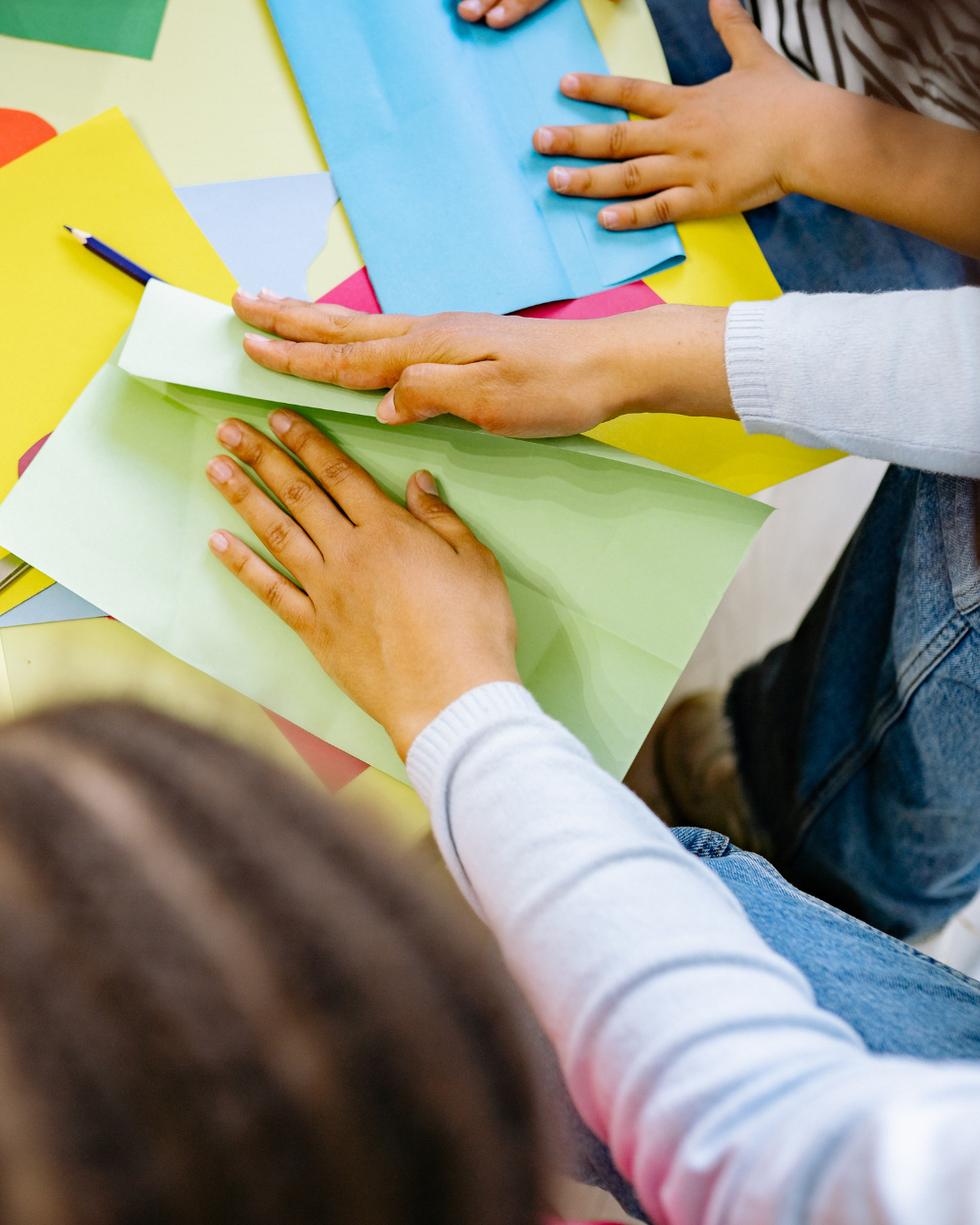 Kinderhände falten buntes Papier.