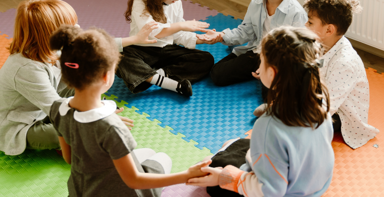 Kinder sitzen im Kreis auf einem Spielteppich.