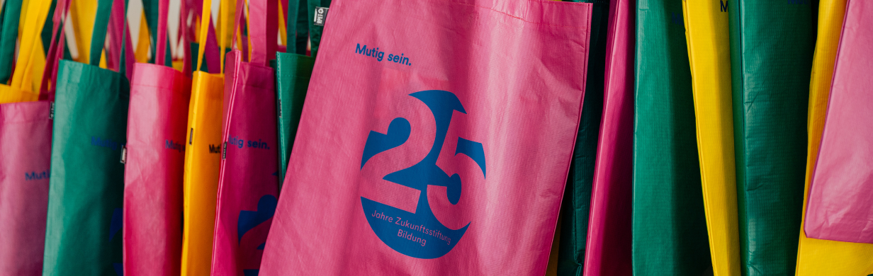 Bunte Taschen mit dem Logo "25 Jahre Zukunftsstoftung Bildung" hängen nebeneinander.