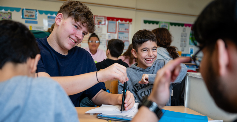 Grundschulkinder und Jugendliche sitzen gemeinsam an einem Tisch, arbeiten und lachen miteinander.