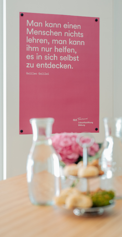 Ein pinkfarbenes Plakat hängt hinter einem Stehtisch.