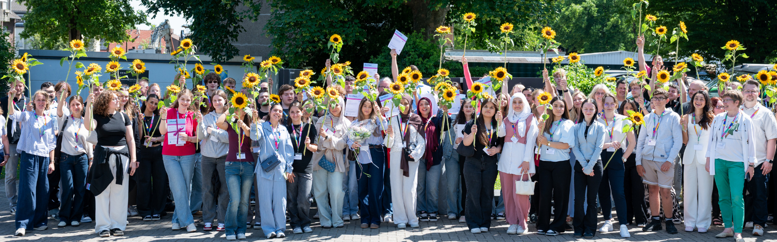 Junge Menschen strecken Sonnenblumen in die Höhe.